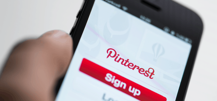 A person holding a phone with the Pinterest app downloaded on the sign-up or log-in screen.