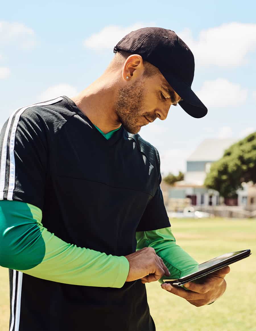 Man in sportswear and a hat looking down at his tablet.