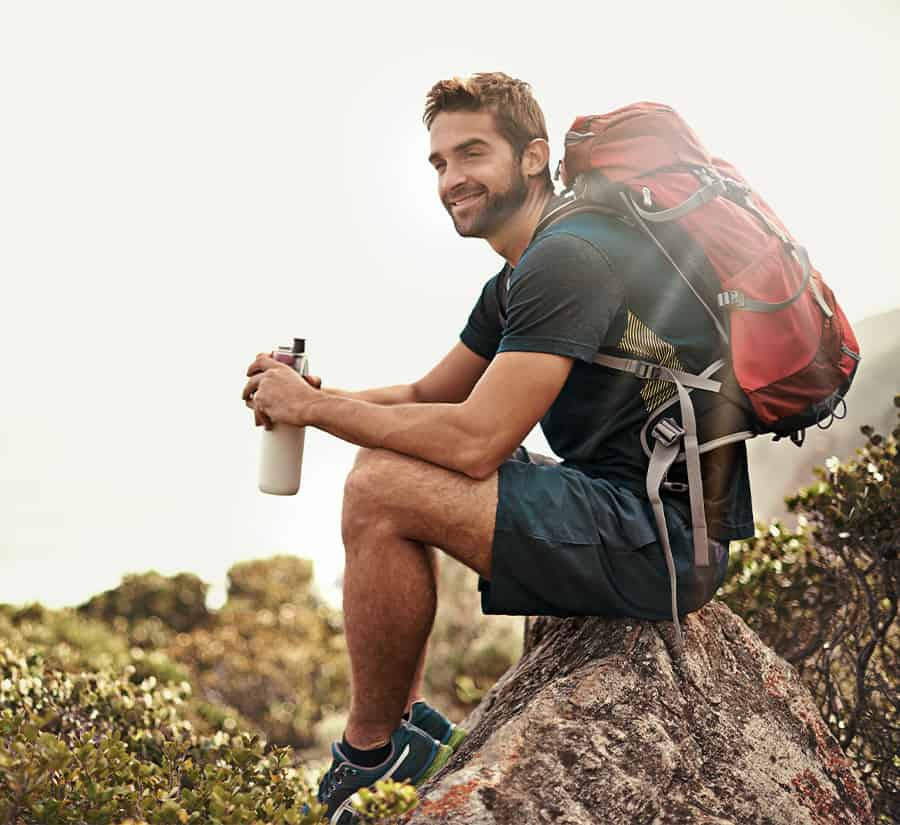 Man with a backpack sitting on a rock taking a break from walking.