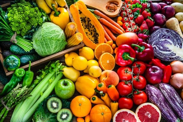Fruits and vegetables are arranged in color order on a table.