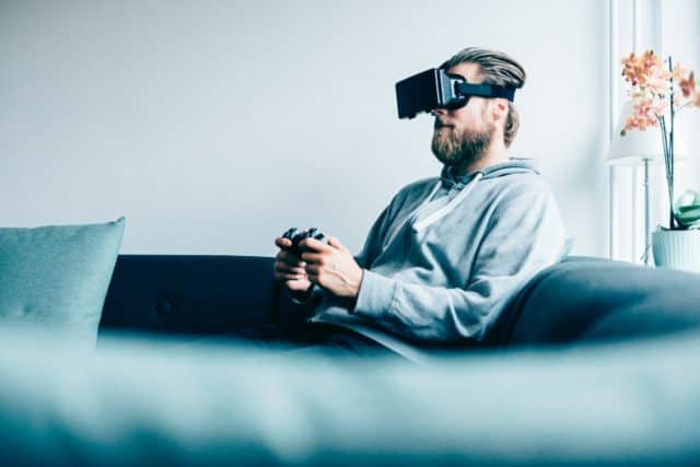 a young man sitting on the couch playing a virtual reality game with a headset.