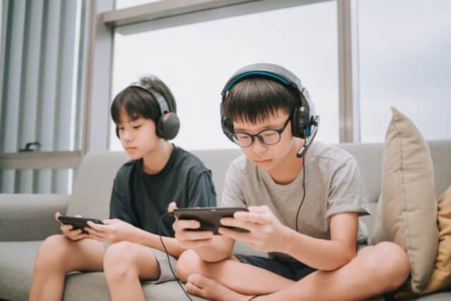 a group of teenagers sitting on the couch with their mobile devices and gaming headgear.