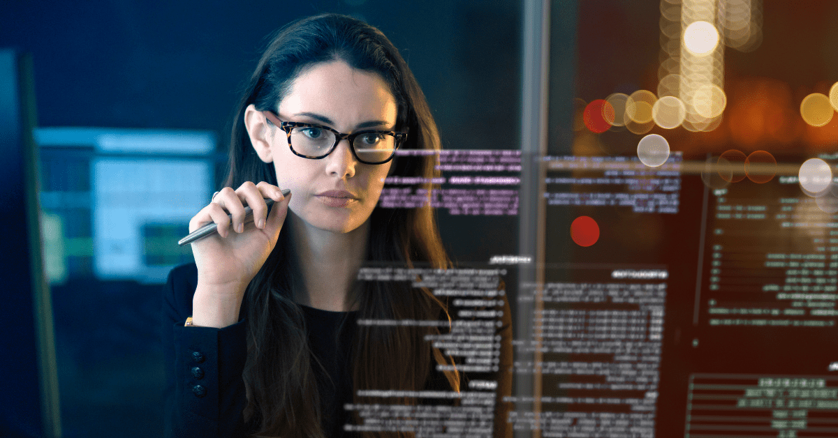 Woman looking at multiple monitors analyzing coding material.