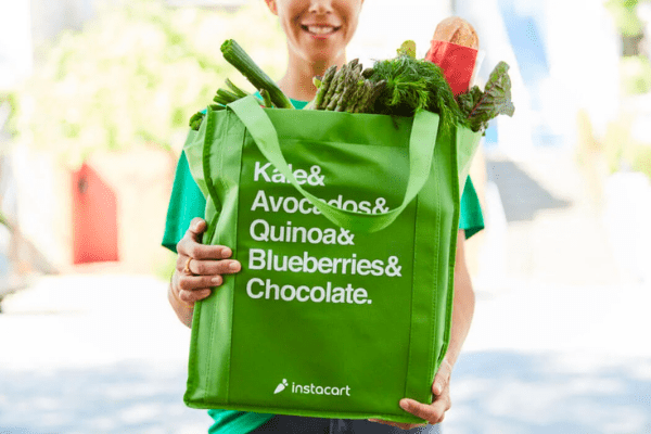 Instacart driver delivering groceries to the customer in a green branded shopping bag.