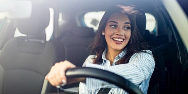 A woman checks her side mirror as she drives a car.