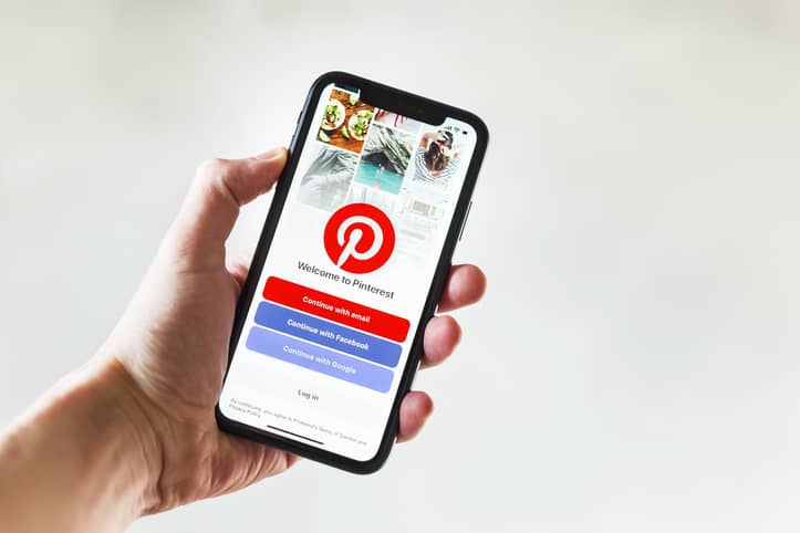 A person’s hand holds a phone with the Pinterest app open on it.