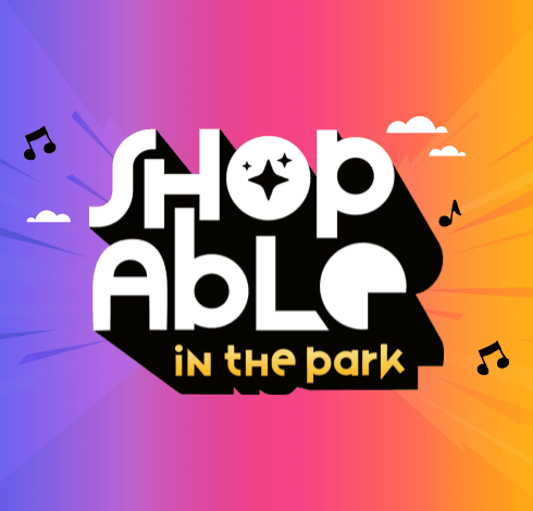 Text graphic reading Shop Able in the Park on a colorful gradient background with music notes, clouds, and sun rays, suggesting a lively outdoor event or festival atmosphere.