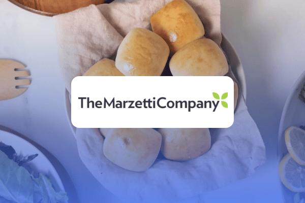A basket lined with a cloth holds seven golden brown dinner rolls. Above the basket, the logo The Marzetti Company with a green leaf is displayed, highlighting a Retail Media Case Study in delicious detail.