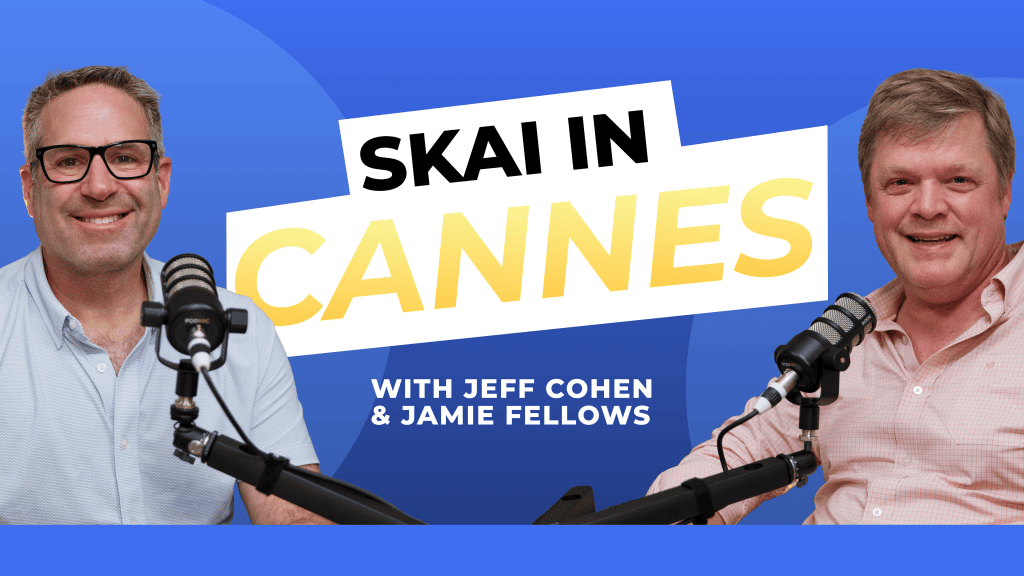 Two men sit in front of microphones, smiling. Behind them, text reads SKAI IN CANNES with Jeff Cohen & Jamie Fellows on a blue background with graphic shapes.