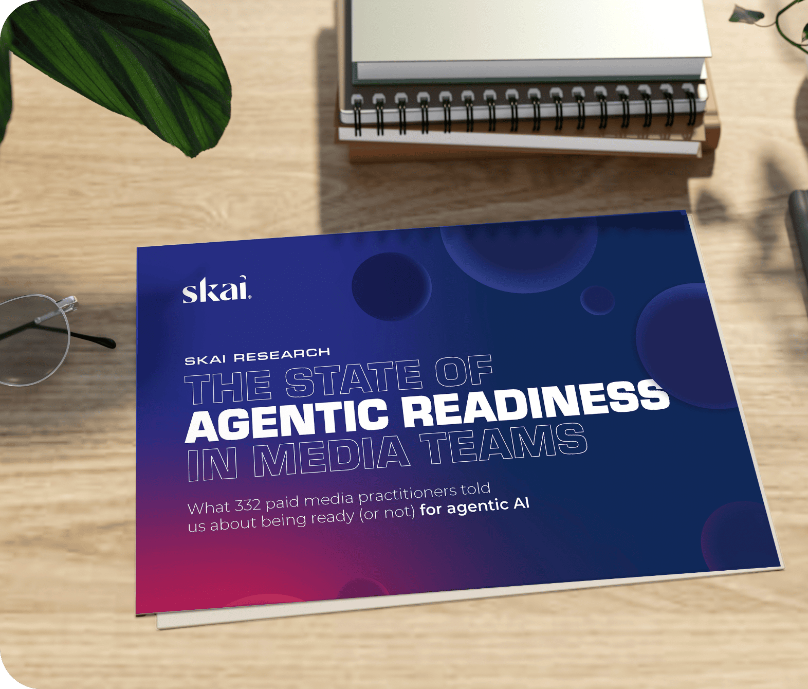 Ein Buch mit dem Titel „The State of Agentic Readiness in Media Teams“ von Skai auf einem Holztisch neben Gläsern, Notizbüchern, einer Pflanze und einem Stift. Das Cover zeigt ein blau-rosa Farbverlaufsmuster mit kreisförmigen Motiven.