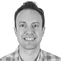 Smiling man with short curly dark hair wearing a plaid shirt, photographed against a plain white background, embodying the importance of omnichannel connectivity in today’s interconnected world.