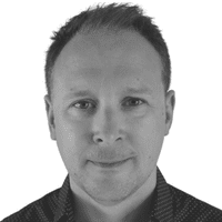 A man with short hair and a slight smile looks directly at the camera, subtly embodying the importance of omnichannel communication in today’s connected world. The image is in black and white with a plain white background.