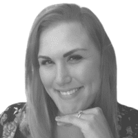 Smiling woman with light hair resting her chin on her hand, looking at the camera. She is wearing a floral-patterned top and a ring on her finger, exuding a thoughtful presence that subtly underscores the importance of omnichannel connections in today’s world. The image is in black and white.