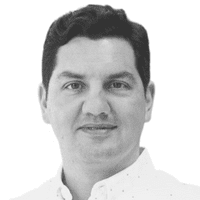 Ein Mann mit dunklem Haar und heller Haut, der ein helles, geknöpftes Hemd trägt, blickt vor einem schlichten weißen Hintergrund direkt in die Kamera und vermittelt dabei auf subtile Weise, wie wichtig Omnichannel-Kommunikation im heutigen Geschäftsumfeld ist.