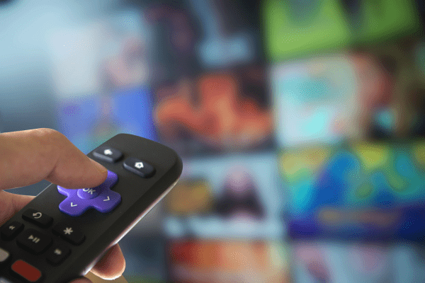 A hand holding a TV remote is pointed at a television screen displaying a grid of colorful, blurred images, suggesting an omnichannel customer experience through a streaming service or channel selection menu.