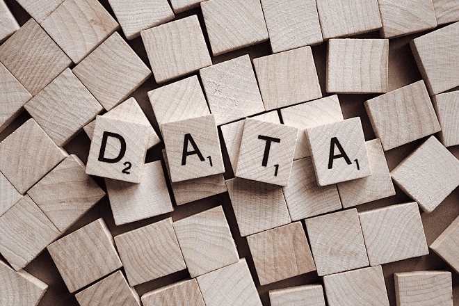 Wooden letter tiles spelling DATA are placed atop a scattered pile of blank wooden tiles, subtly underscoring the importance of omnichannel strategies in organizing and utilizing information effectively.
