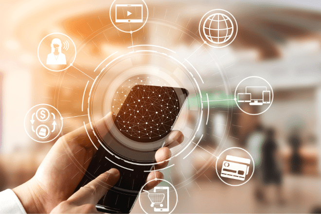Une personne tient un smartphone entouré d'icônes numériques représentant des services en ligne tels que la banque, le shopping, la vidéo et Internet, sur un fond d'intérieur flou, soulignant ainsi l'importance des expériences omnicanales dans le monde connecté d'aujourd'hui.