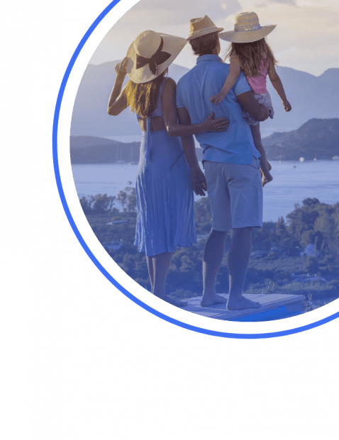 A woman, man, and child in summer hats overlook a scenic lake and mountains, standing together on a platform, viewed from behind.