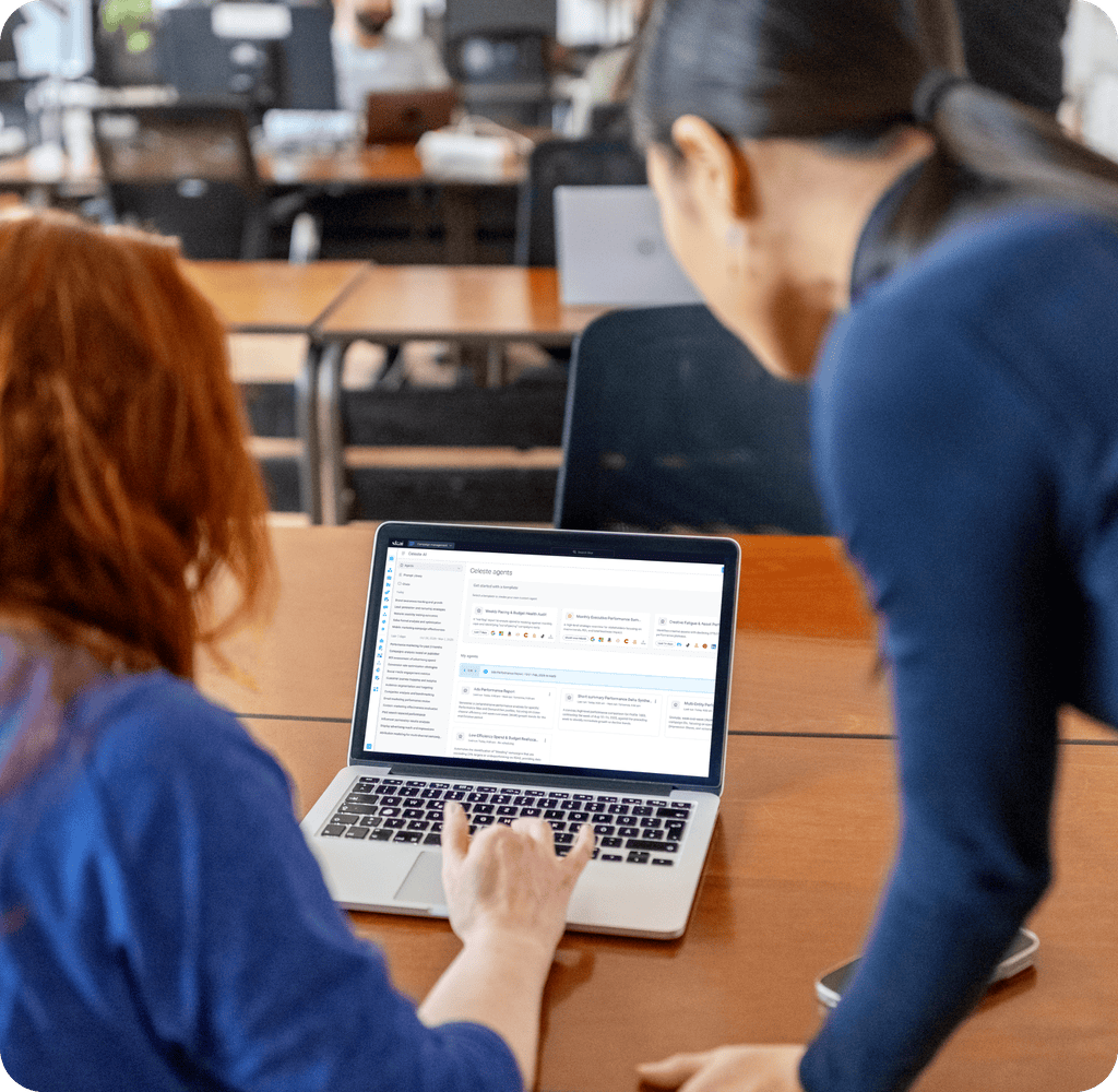 Two people look at a laptop screen displaying colorful charts and data in an office setting with empty desks in the background, as they discuss strategies using AI marketing consulting services.